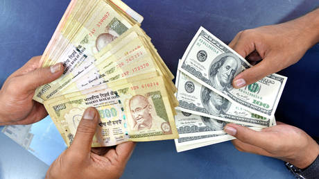FILE PHOTO. Indian customers at a foreign exchange outlet pose for a photo as they exchange Indian rupees (L) for US dollars in Bangalore on August 24, 2013.